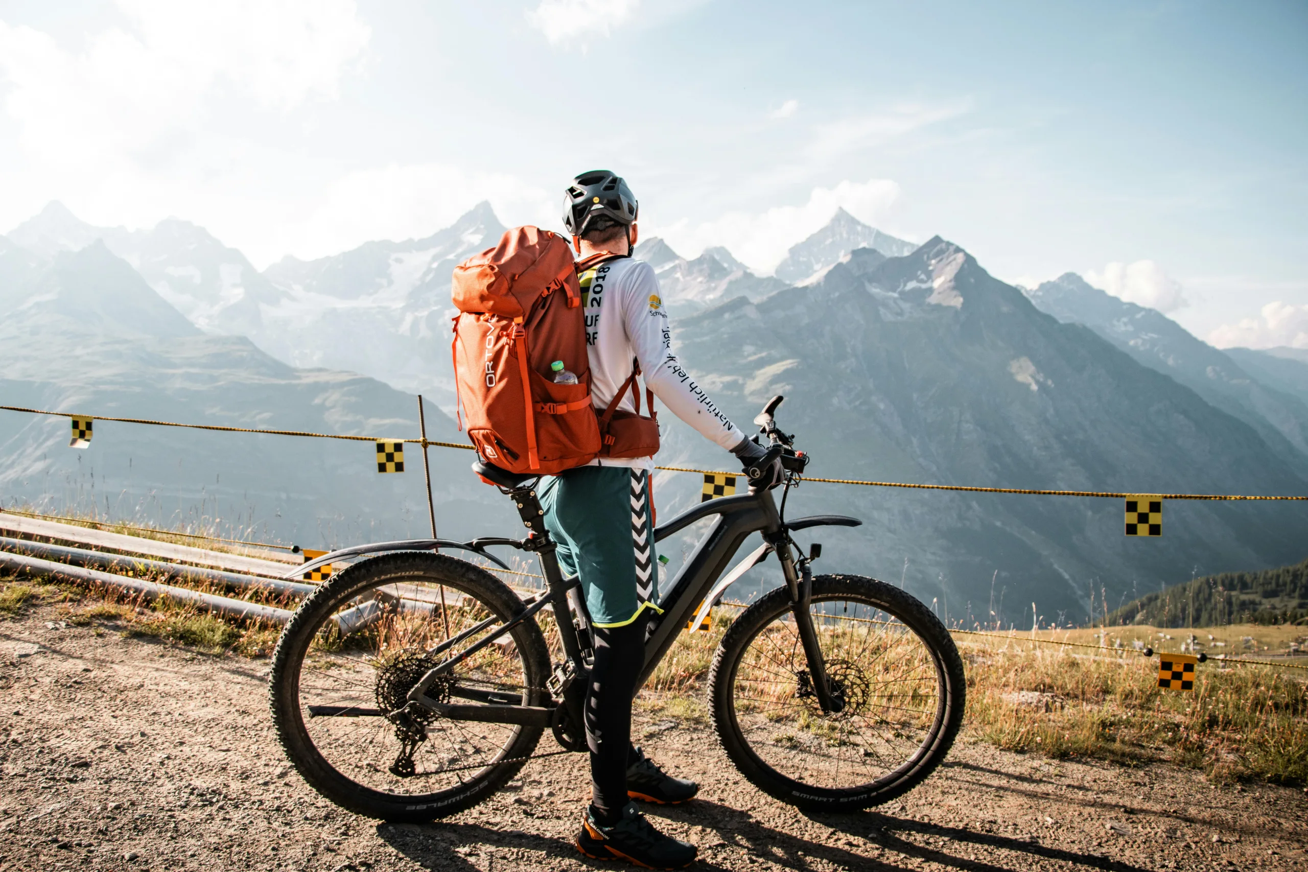 A man on a bike stops on the side of a road to admire a mountain view.