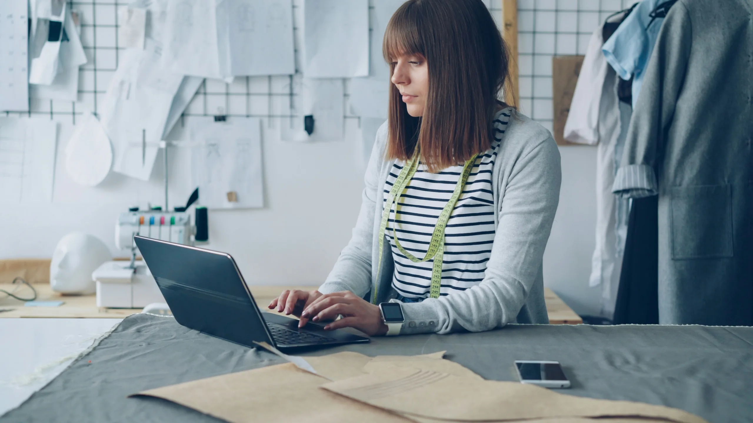 A woman in the fashion and apparel industry sits at a desk and types on a laptop.