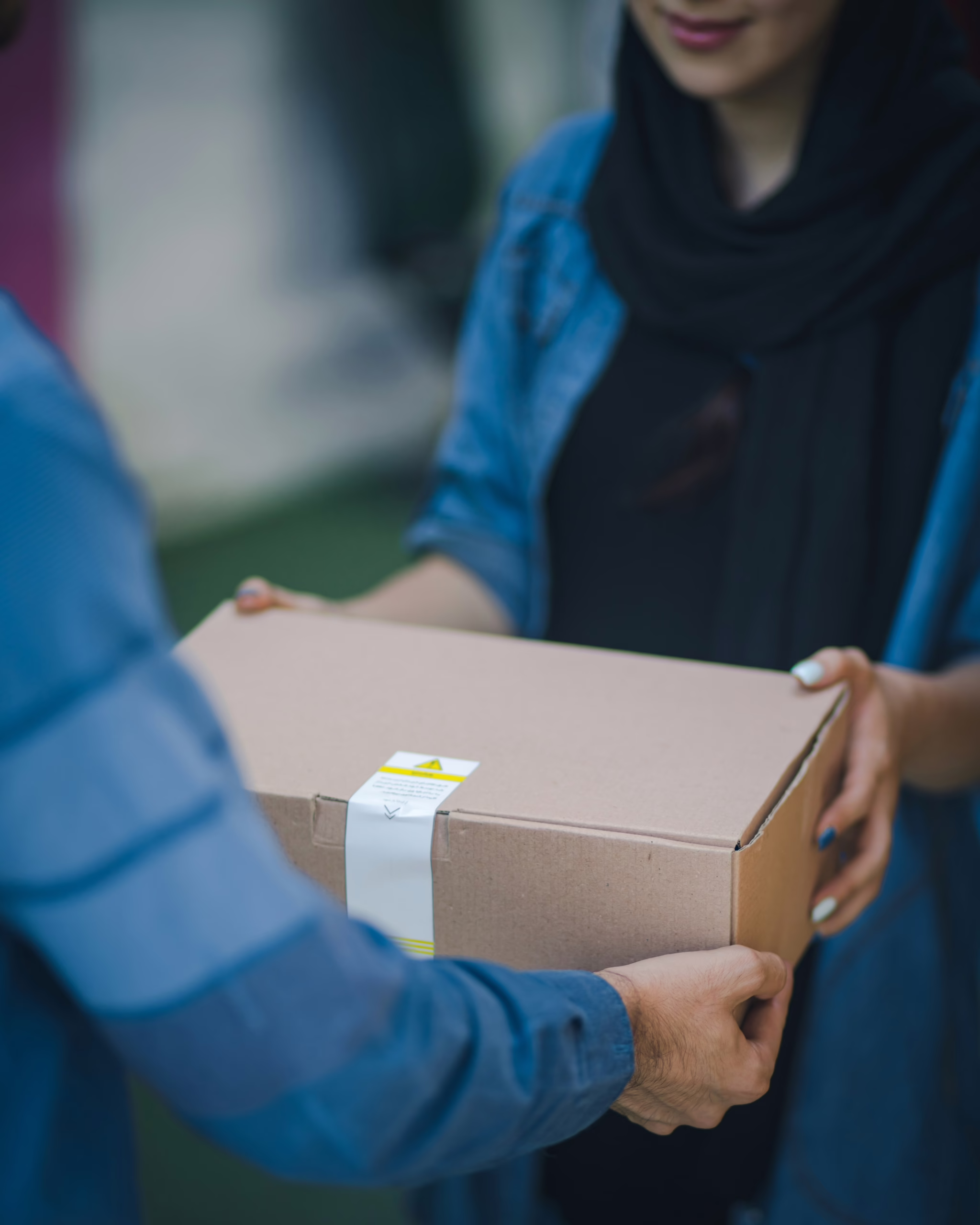 A delivery person passes a cardboard box parcel to the recipient.